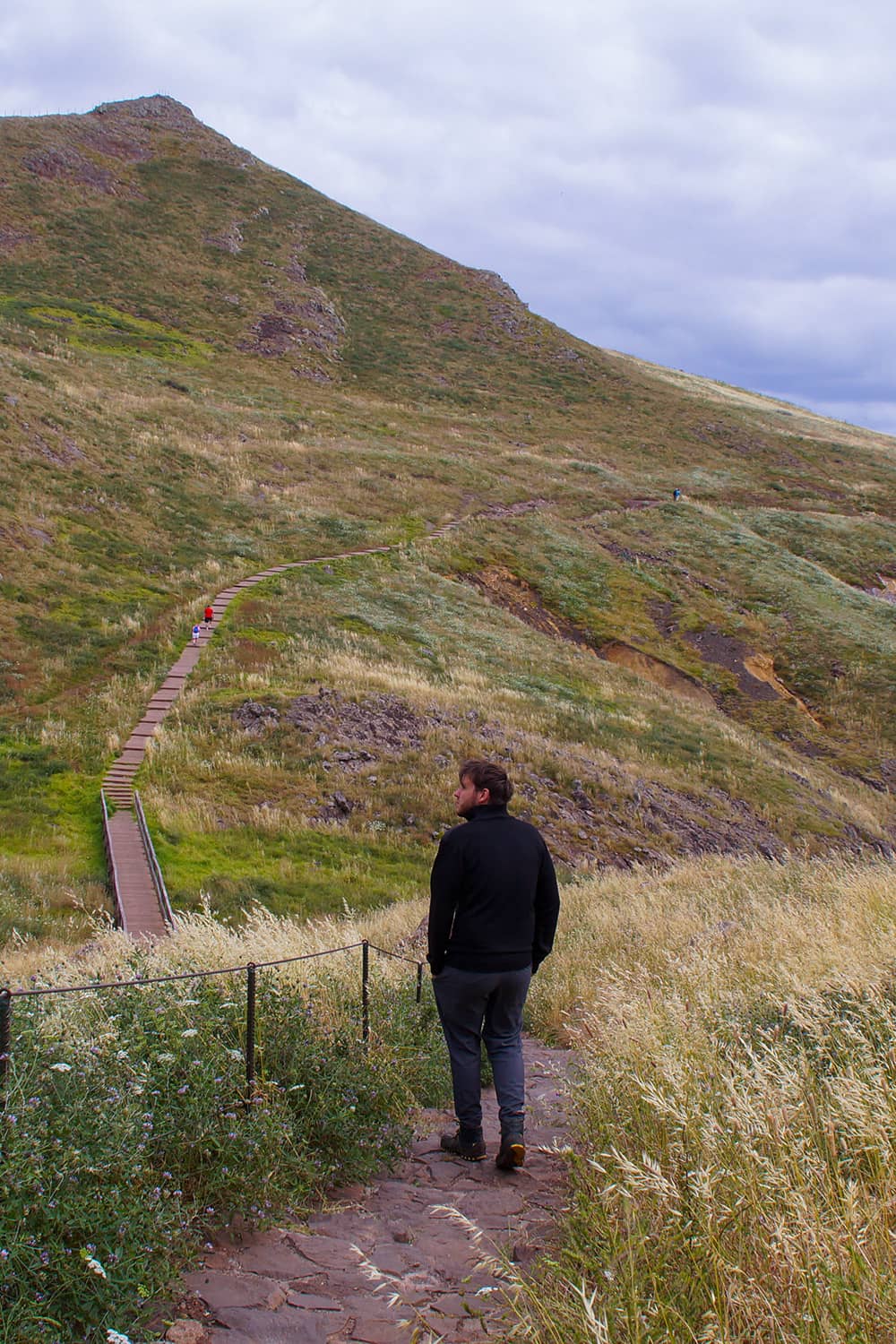 Man walking on a hiking trail through grassland on cliffs near the ocean.