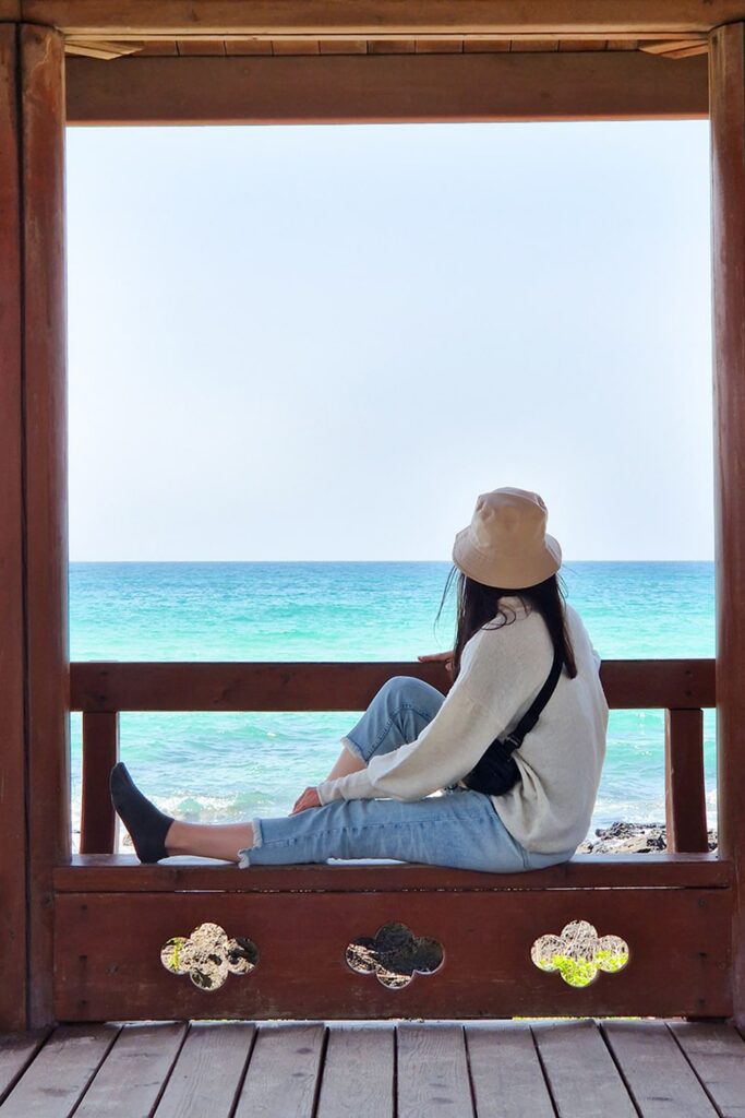 girl sitting on wooden bench looking out at the blue sea on Jeju island