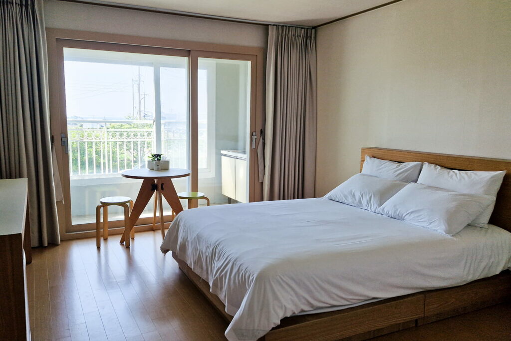 Hotel room with a bed on the right and table in front of window on Jeju island