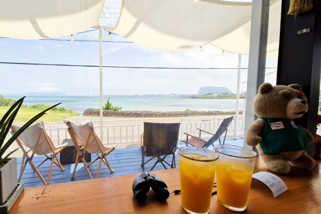 two tangerine juices on a table with views of Jeju island in the background