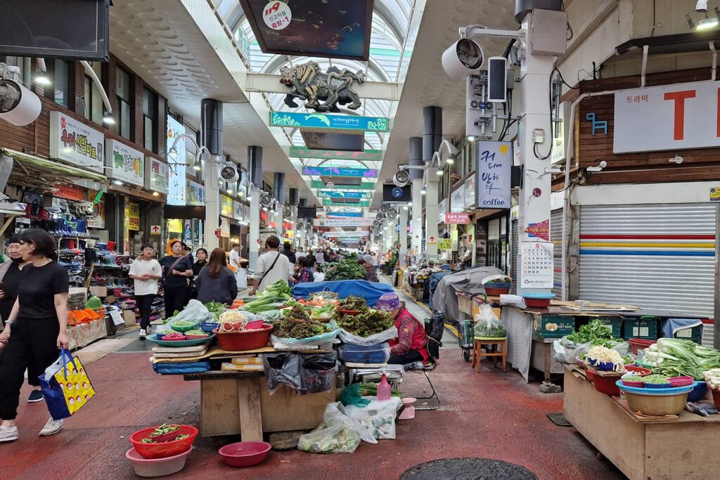 produce stalls and people walking through seogwipo olle market