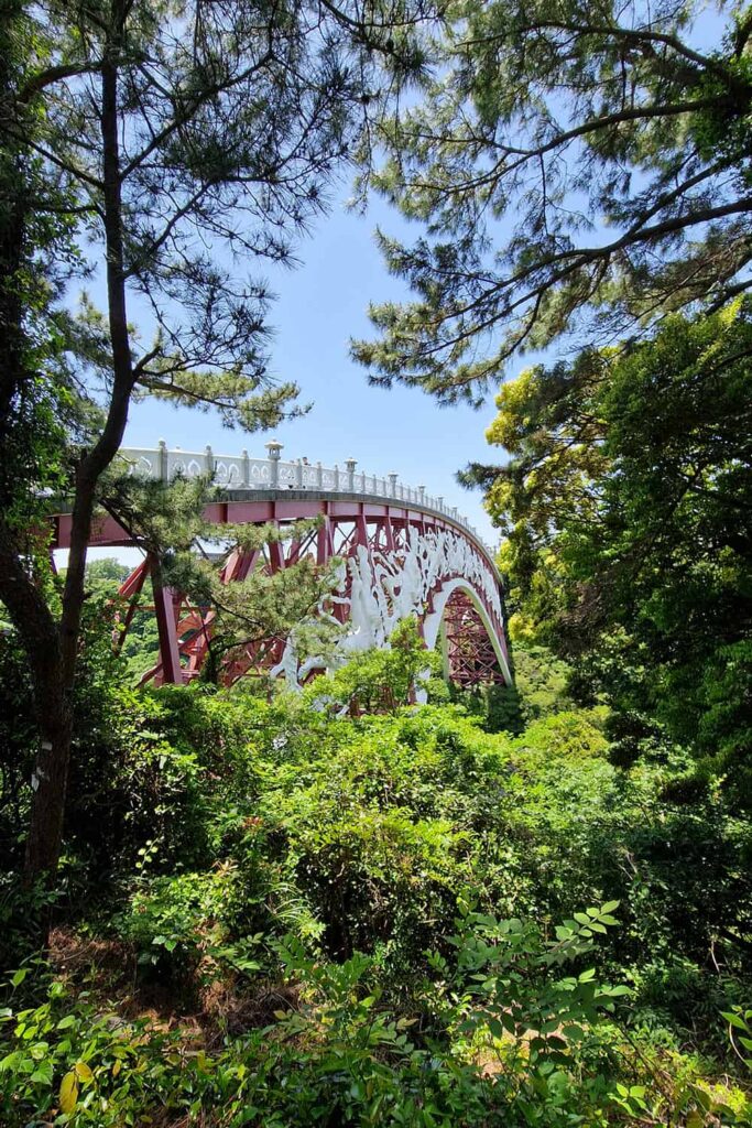 Huge red bridge connecting to sides of a forest.