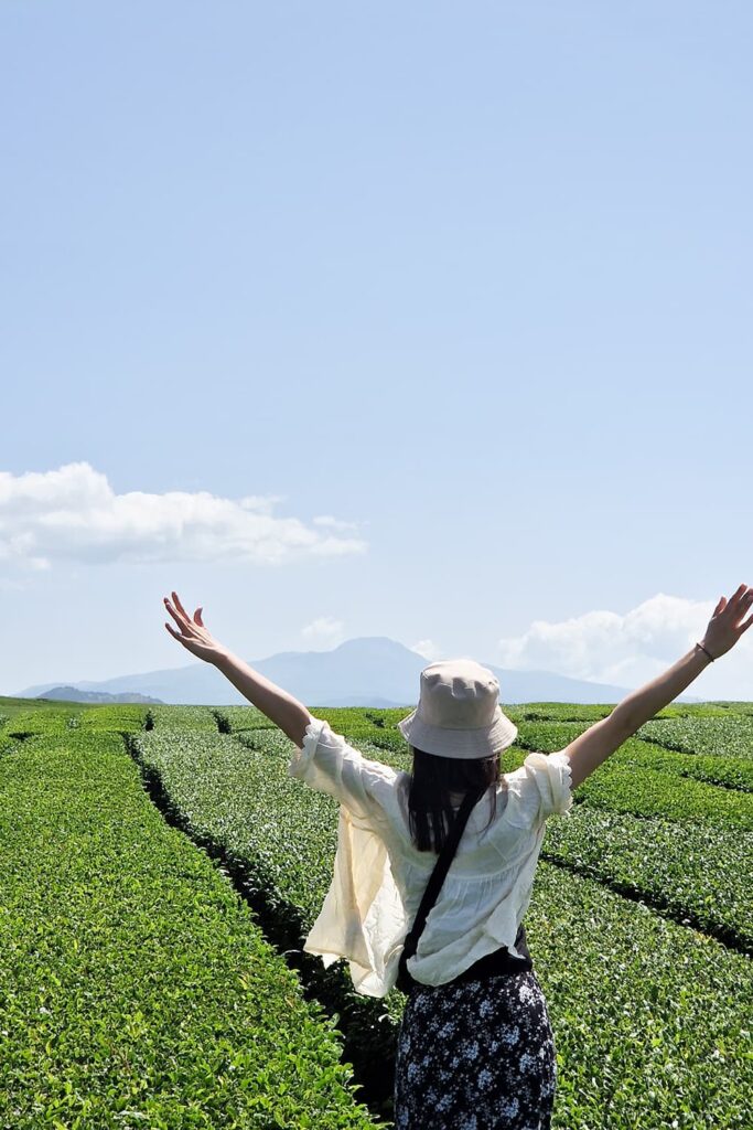 Girl striking a pose in front of tea fields with a mountain in the background.