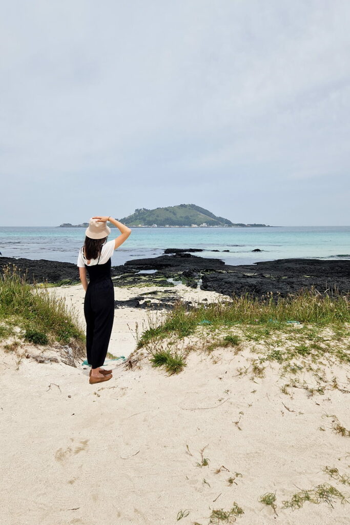 Woman standing on a beach looking out over the ocean.