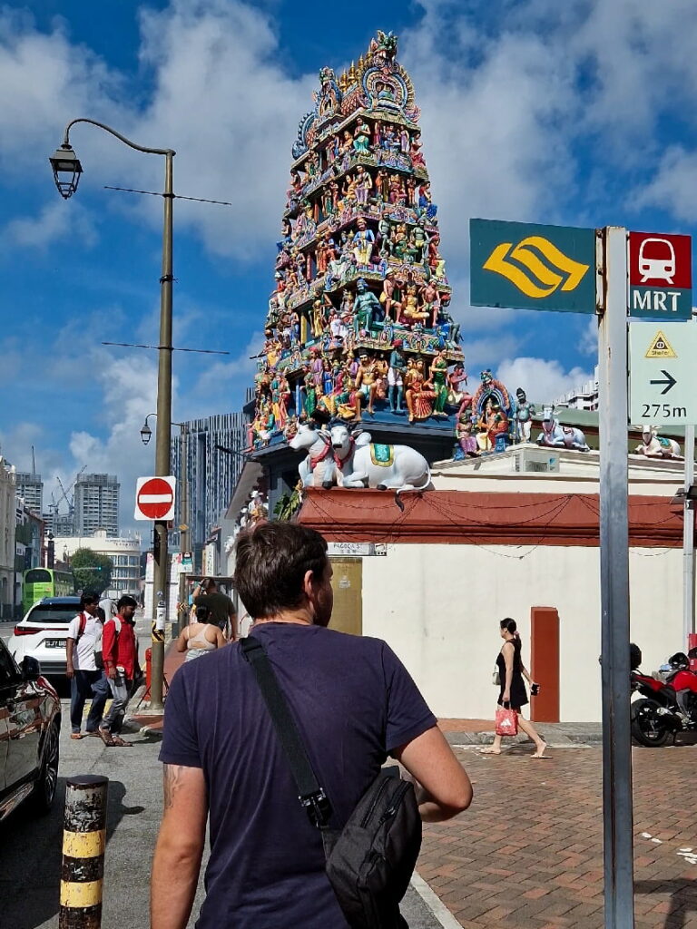 Man going past an hinduistic temple and an MRT sign.