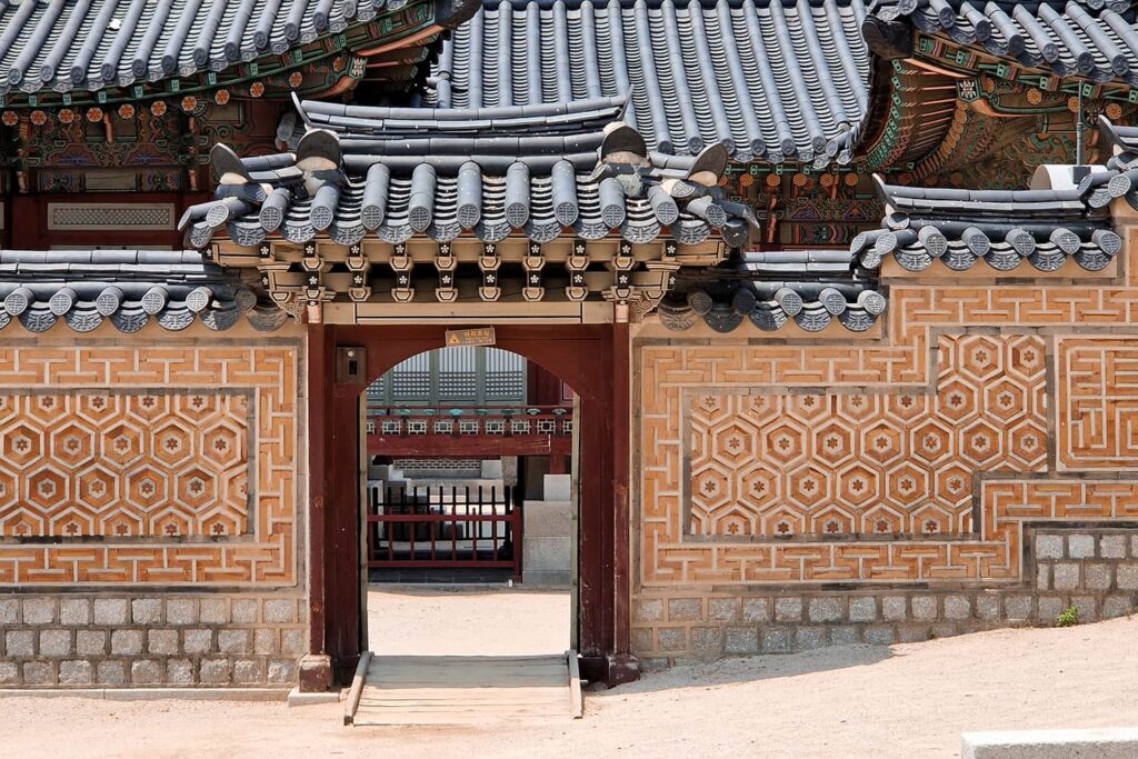 A yellow ornate korean palace wall with a small gate leading to a small side building of the palace.