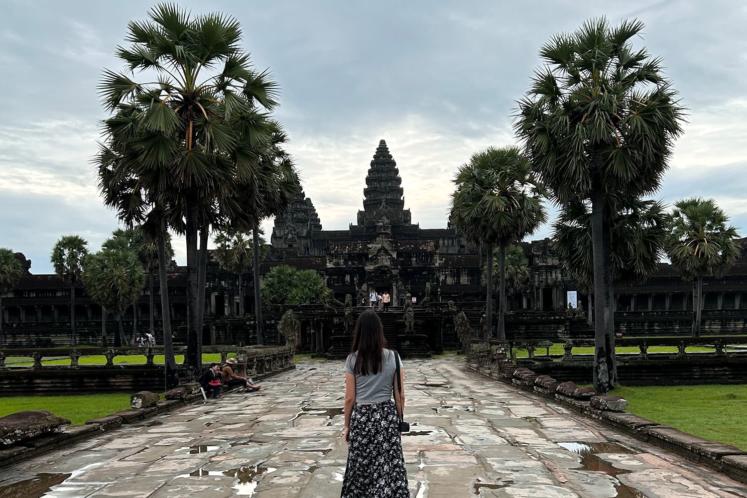 Girl walking to the Angkor Wat temple on a walkway surrounded by palm trees.