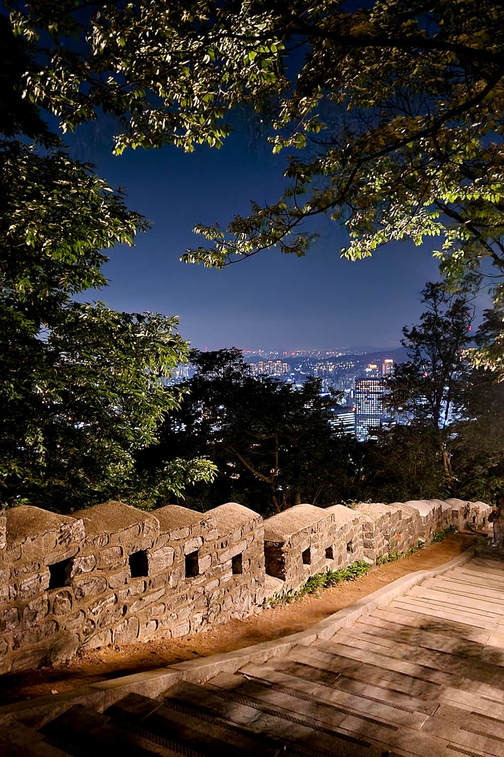 Stairs going down a mountain during night-time with a view over the city of Seoul.