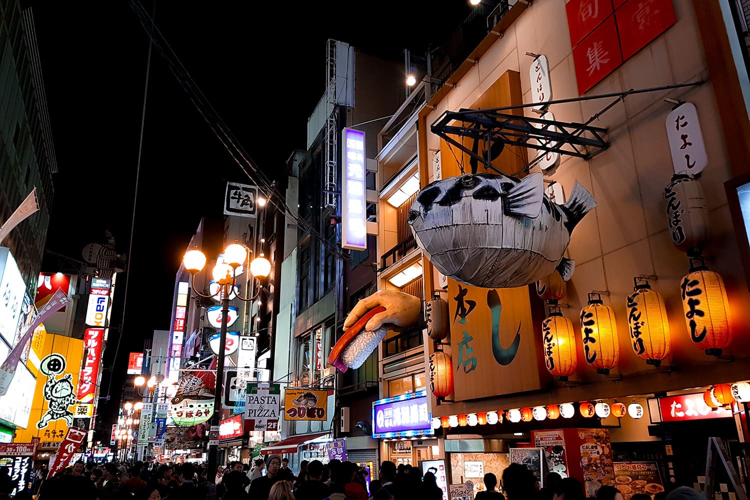 A street in Dotonbori Osaka with colorful statues on the walls.