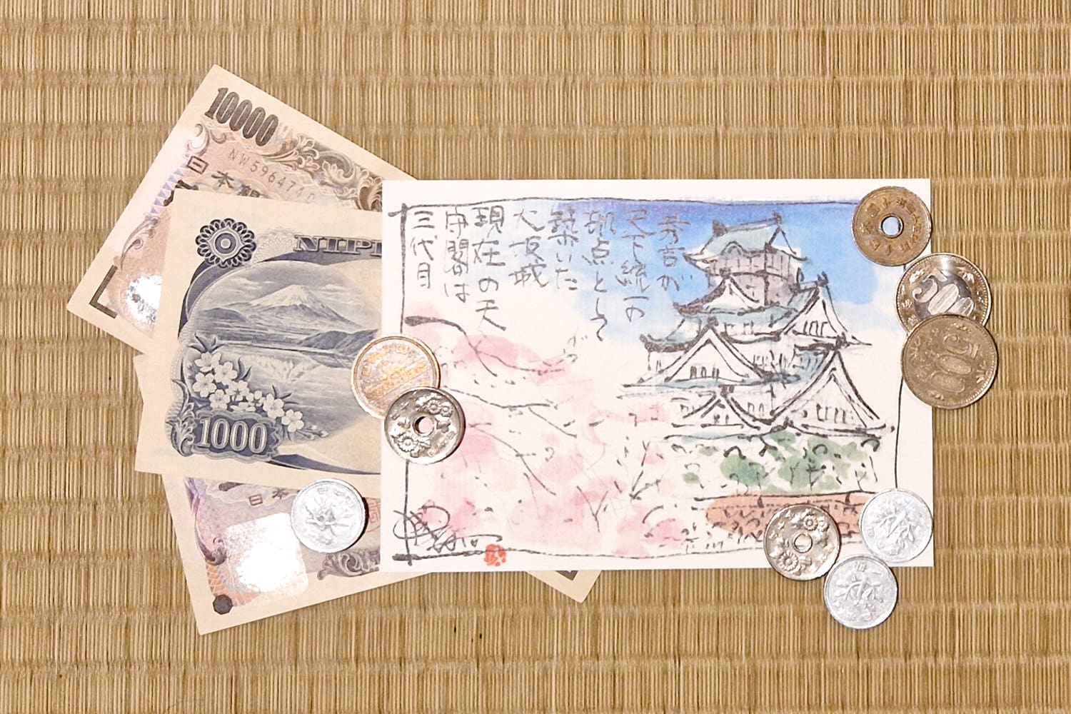 Some Japanese Yen coins and bills with a postcard featuring Osaka Castle.