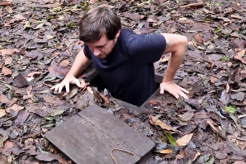 A man being half emerged in the famous cu-chi tunnels in vietnam while trying to enter himself.