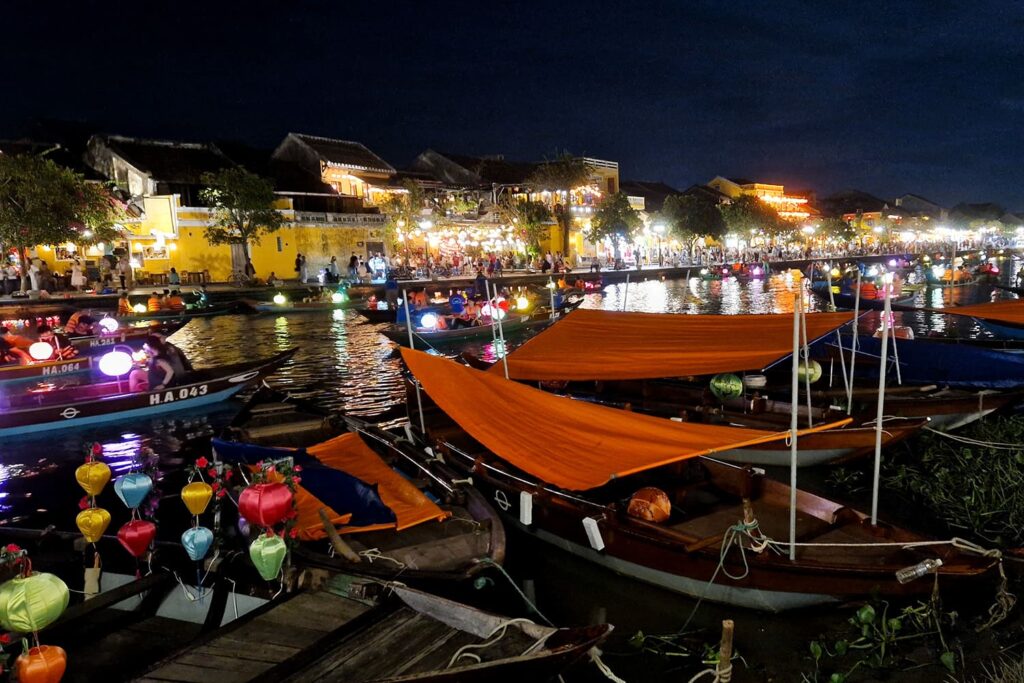 The canal in Hoi An by night, filled with lanterns and boats driving through.