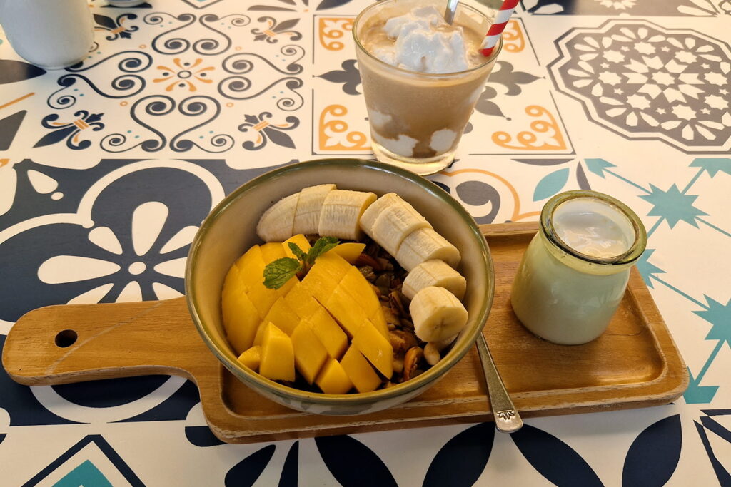 A healthy fruit bowl with a yoghurt and a coconut coffee.
