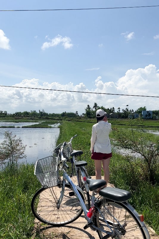 Woman with a bicycle standing in front of a rice field, enjoying the view in Hoi An, Vietnam.